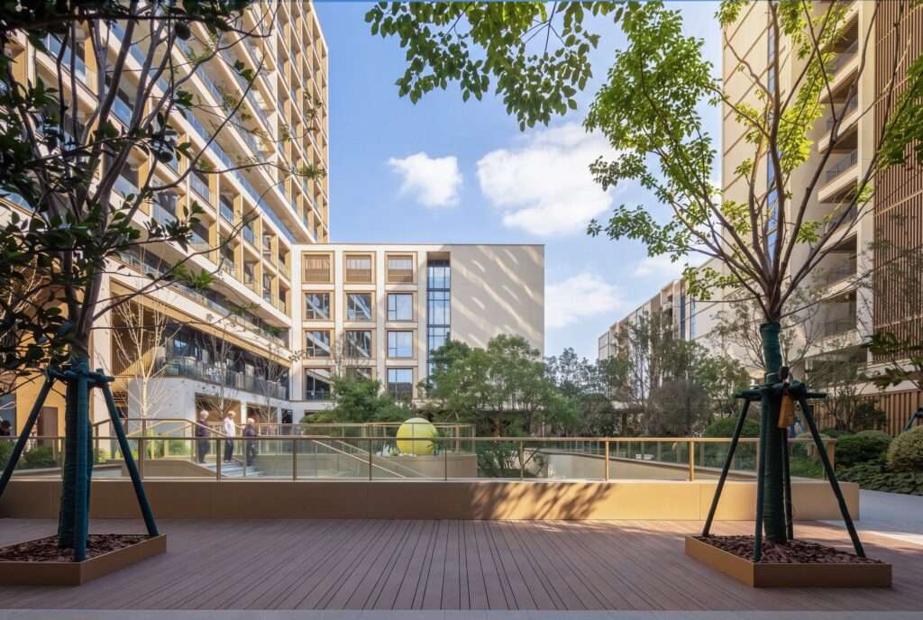 Courtyard garden with timber decking and planted trees framed by modern multi-story senior living residential towers under a clear blue sky.