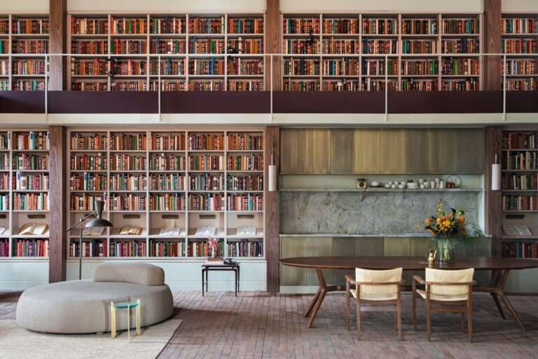Double-height central library with wall-to-wall wooden bookshelves integrated beside a dining table and kitchen niche in Casa Curral Cileiro Alvorada.