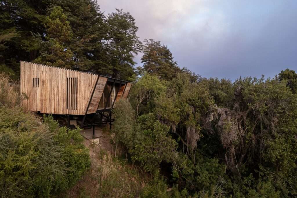 Cantilevered wooden studio volume elevated on black steel columns over a steep forested slope at Casa El Trébol.