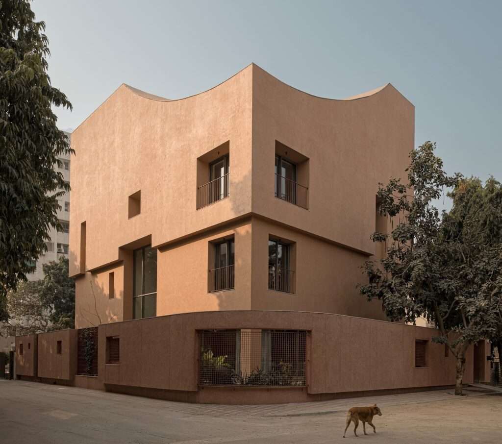 Exterior street view of LJ House in Ahmedabad showing a monolithic earth-toned plaster facade with deep window recesses and a curved parapet roofline.