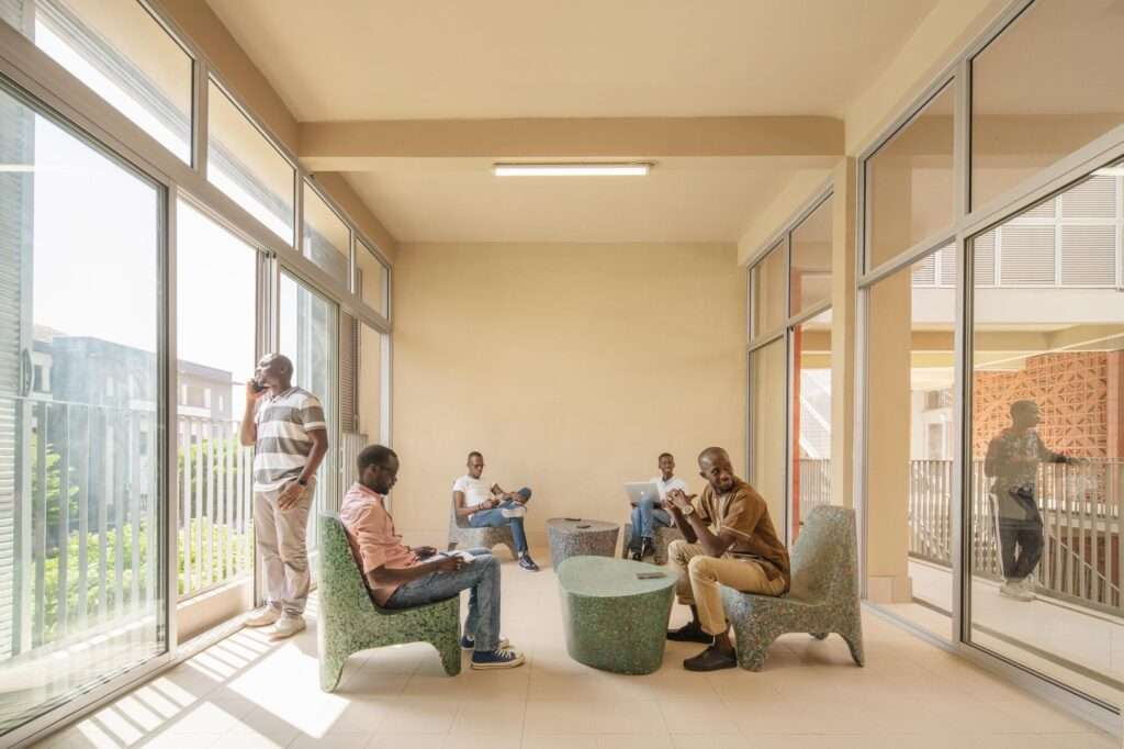 Students relaxing inside a naturally lit study lounge with large glass windows and recycled terrazzo furniture.