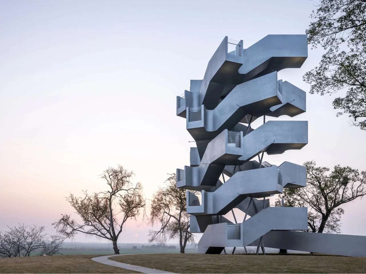 Exterior view of Qinghu Migratory Bird Observation Tower showing twin interlocking steel spiral staircases against a sunset sky.