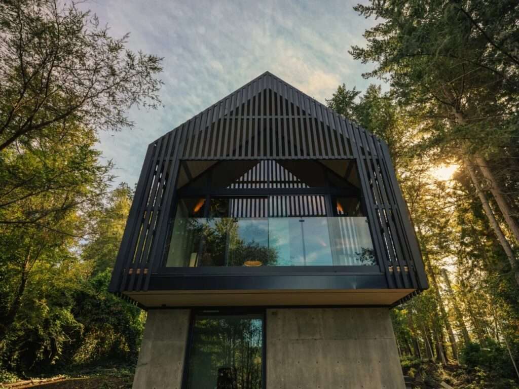 Low-angle exterior view of Forest Studio showing a concrete lower base supporting a dark timber cantilevered upper level with glass balcony railing.
