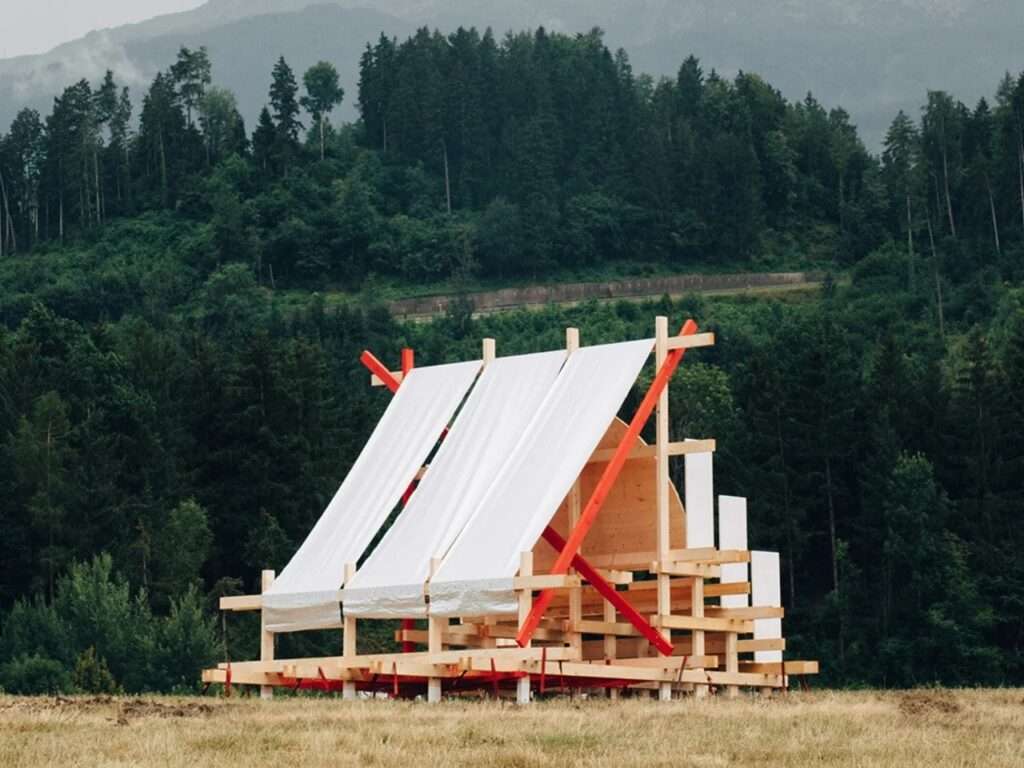 Perspective view of the Gabonsa Pavilion on a grassy slope with a dense green forest and large, misty mountains in the background under an overcast sky.