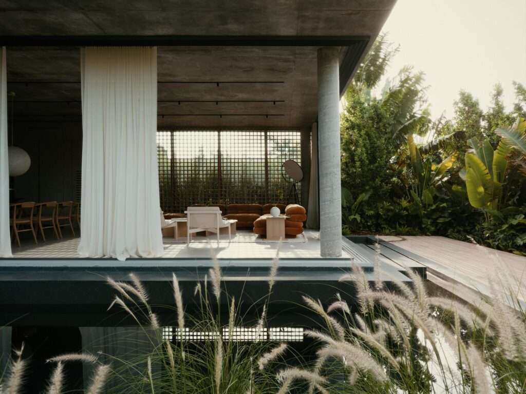 Open-plan living room with plush brown modular sofa and wooden lattice screen opening to an outdoor reflection pool.