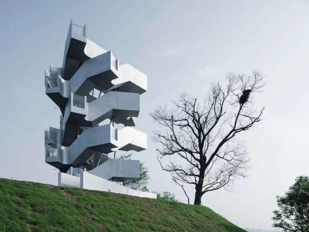 Low-angle view of the Qinghu bird observation tower on a grassy hill beside a tall tree with a bird nest.
