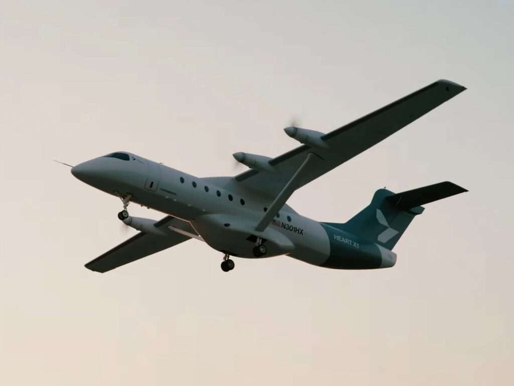 Bottom-up low-angle view of the Heart X1 aircraft flying overhead with its landing gear deployed against a clear sky.