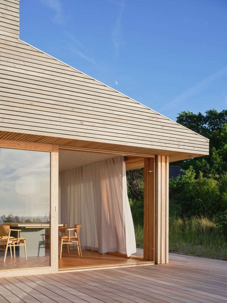 Close-up view of the wooden timber cladding roof, sliding glass doors, and outer deck of Rågeleje House overlooking nature.