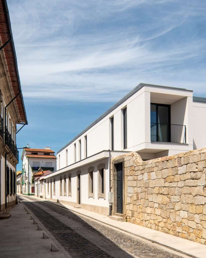 Narrow cobblestone street in Vila do Conde showing a single-story restored historic facade beneath a recessed white modern story.