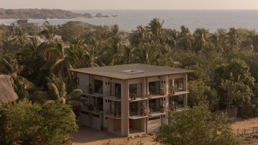 High-angle aerial view of Suuel Living residential building surrounded by dense palm trees with the ocean visible in the background.