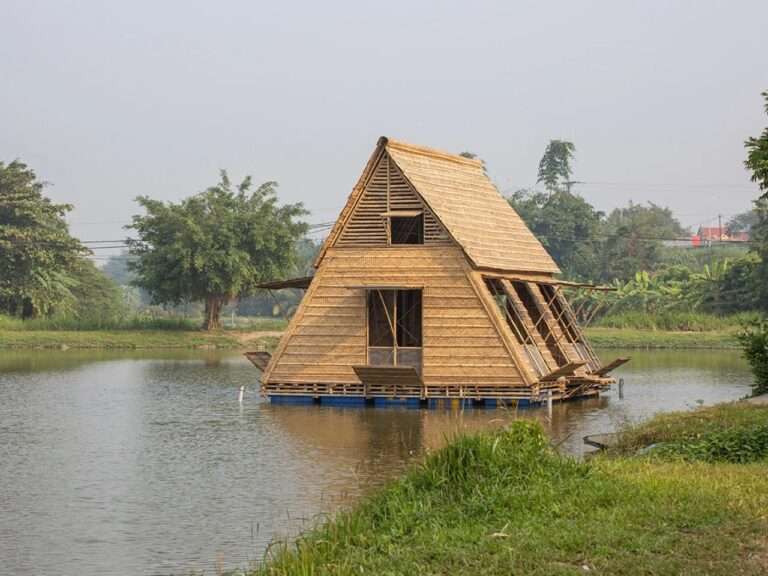 The Floating Bamboo House by H&P Architects, a triangular structure made of bamboo on a platform of blue barrels, floating on calm water in the Mekong Delta, with green banks and trees in the background.