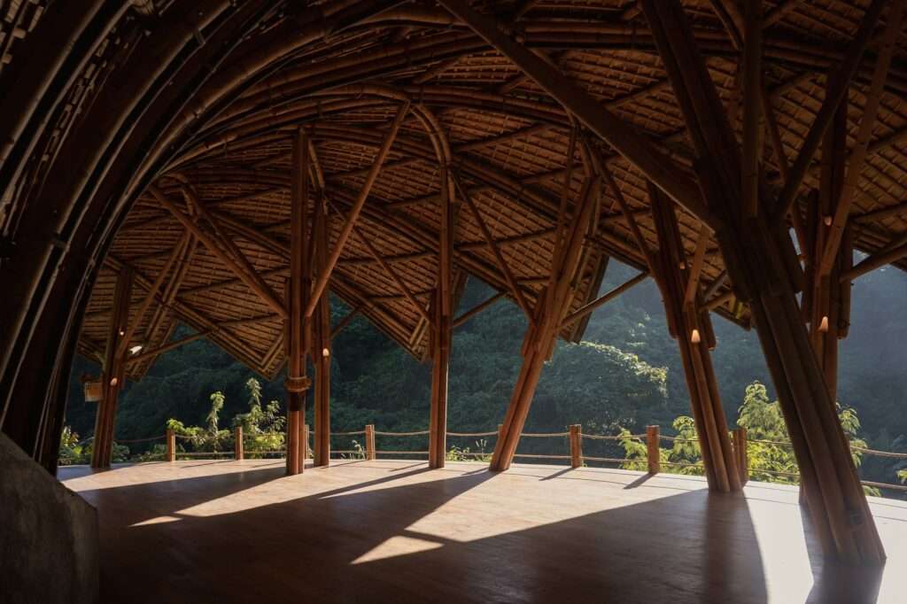 Interior view of Lotus Shala featuring open wooden flooring, arched bamboo columns, and a panoramic view of lush greenery.