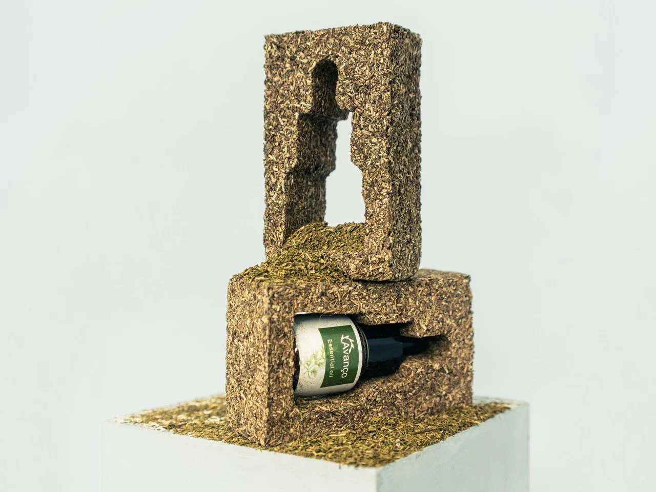 Two stacked custom molded blocks made from compressed agricultural plant waste holding a dark glass Avanço essential oil bottle.