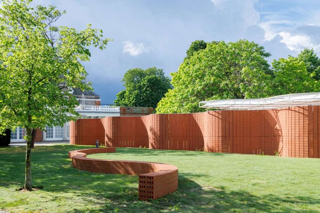 Red brick curved bench and pavilion wall in grassy park daytime