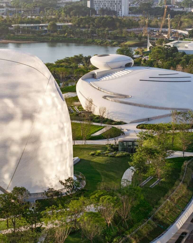 Aerial perspective of smooth, white organic pavilion roofs integrated with green lawns and surrounding water bodies at Shenzhen Bay Culture Square.