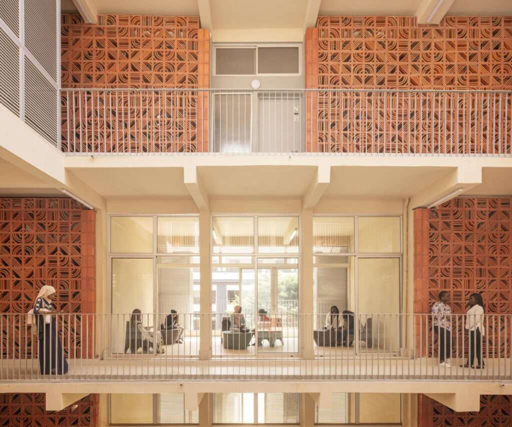 Multi-story courtyard facade showing glazed study rooms flanked by patterned terracotta breeze-block walls and walkways.
