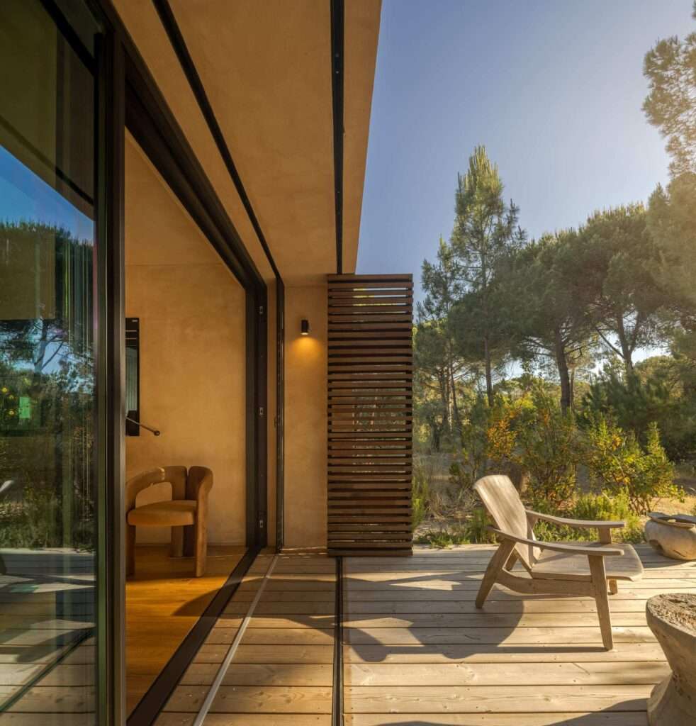 Wooden outdoor terrace with lounge chair opening into bedroom interior at Muda L13 House.