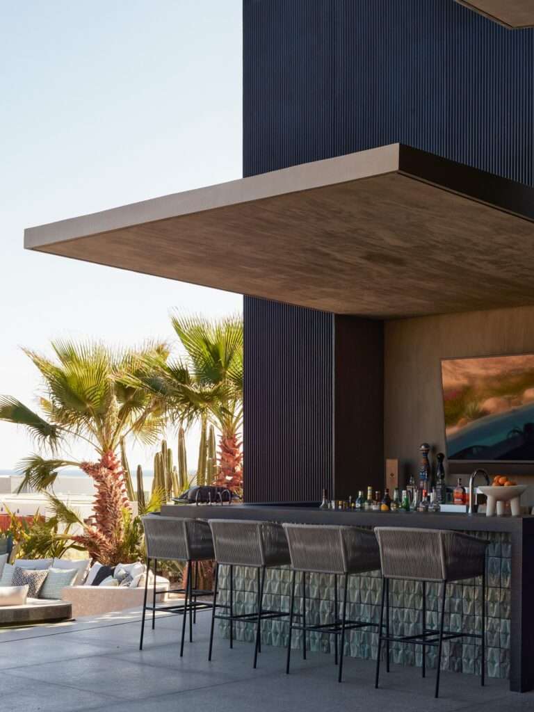 Outdoor sheltered bar area under a cantilevered concrete roof with tiled counter front and view of palm trees.