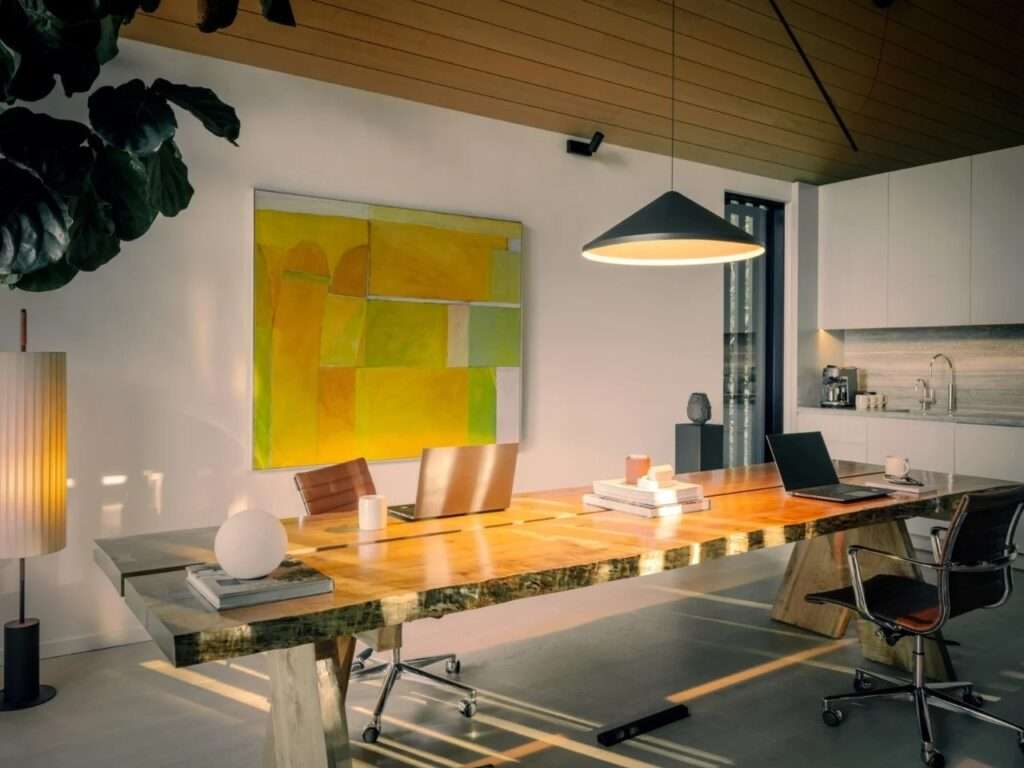 Interior of Forest Studio featuring a long live-edge wooden conference table, hemlock wood ceiling, modern pendant light, and vibrant artwork.