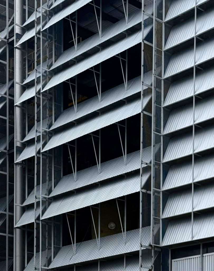 Architectural detail of layered, angled corrugated steel louvers and supporting steel frame modules on a building facade.
