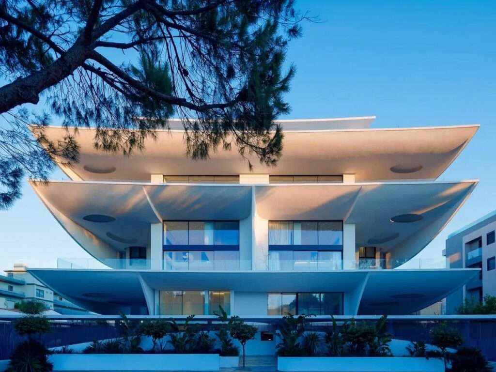 Front elevation of Rive en Hospense building showing organic white layered curved balconies with recessed lighting at dusk.