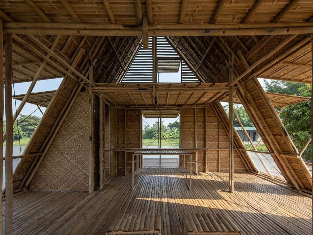 Interior of the Floating Bamboo House, looking from the main floor towards the raised loft, showing all-bamboo construction, woven walls, bamboo furniture, and open triangular frames with outside views.