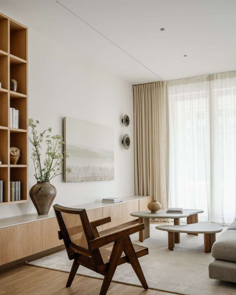Detail view of the living room seating arrangement with a mid-century wooden armchair, organic stone coffee tables, and built-in shelving.