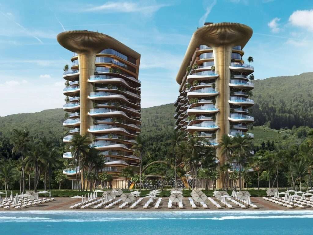 Front beachfront view of Montemar Residential towers set against lush green mountains in Gonio with sun umbrellas along the coast.