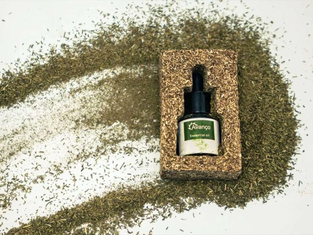 Top-down view of an Avanço essential oil bottle encased in a rectangular compressed fiber cushion surrounded by loose dried rosemary leaves.