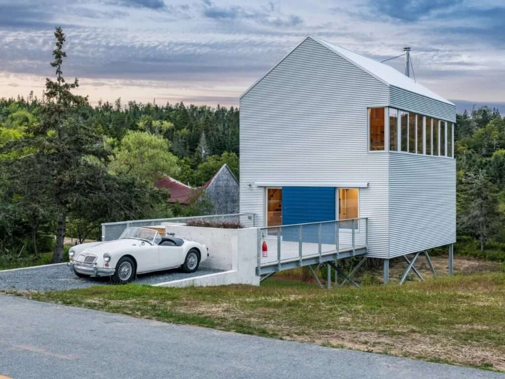 Exterior view of the elevated Skybox residence featuring corrugated Galvalume metal cladding, a bridge entry with a vintage sports car, and steel pilotis.