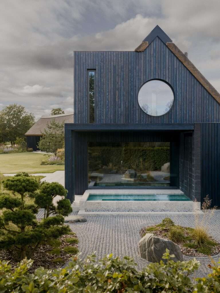 Modern exterior facade with dark wood siding, circular window, built-in outdoor plunge pool, and raked gravel Japanese zen garden.