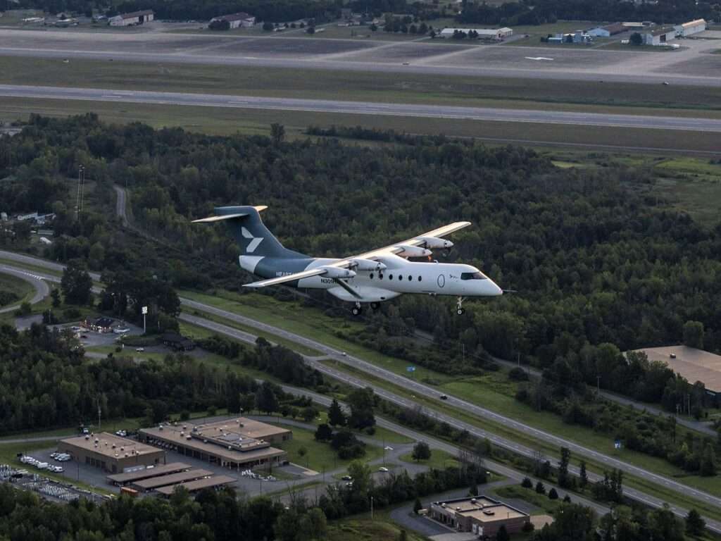 Aerial view of the Heart X1 regional demonstrator flying over green landscape near an airport runway.
