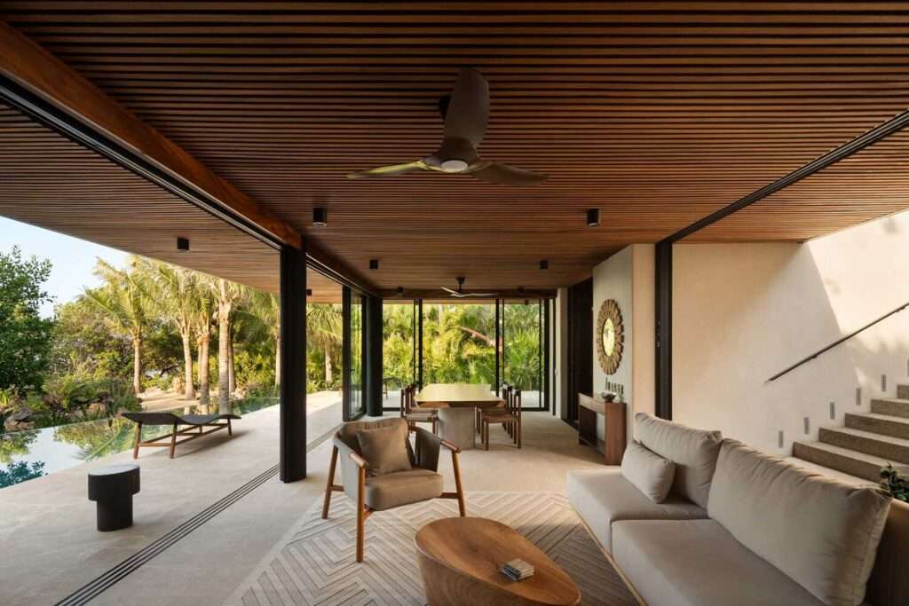 Open-concept living and dining area with seamless access to an outdoor pool, featuring a wooden slatted ceiling and minimalist furniture.