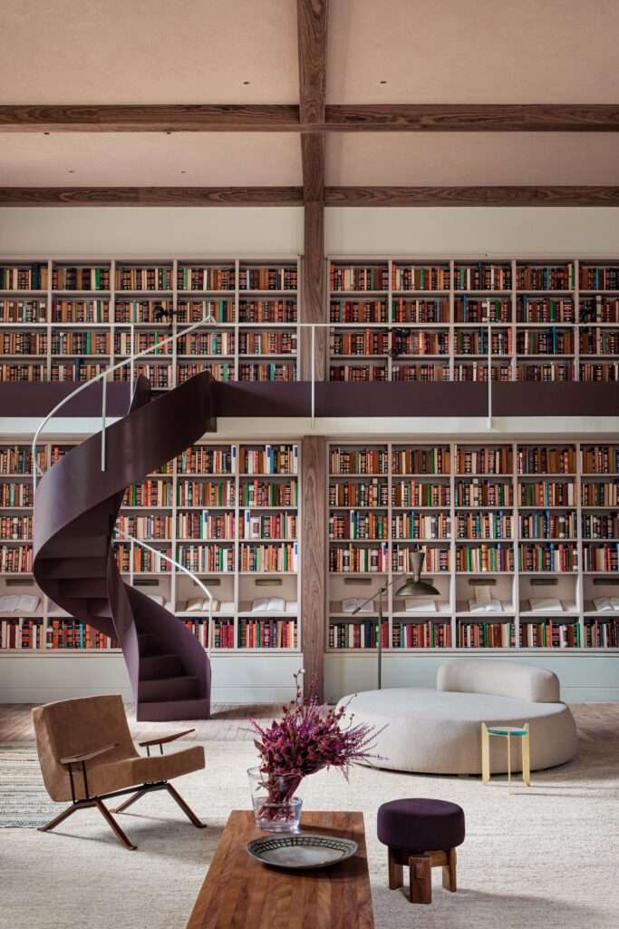 Dark purple spiral staircase ascending to a mezzanine library with exposed timber ceiling beams and plush lounge seating.
