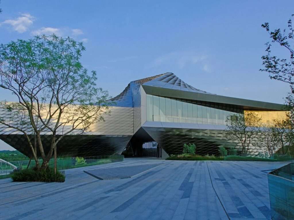 Exterior view of the Chengdu Pavilion's polished metal facade and glass envelope facing a paved stone plaza.