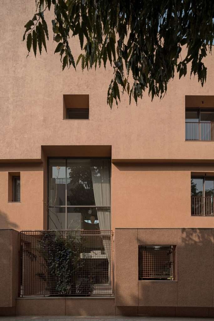 Close-up architectural elevation of LJ House featuring textured terracotta plaster walls, recessed glazed openings, and metal security grilles.