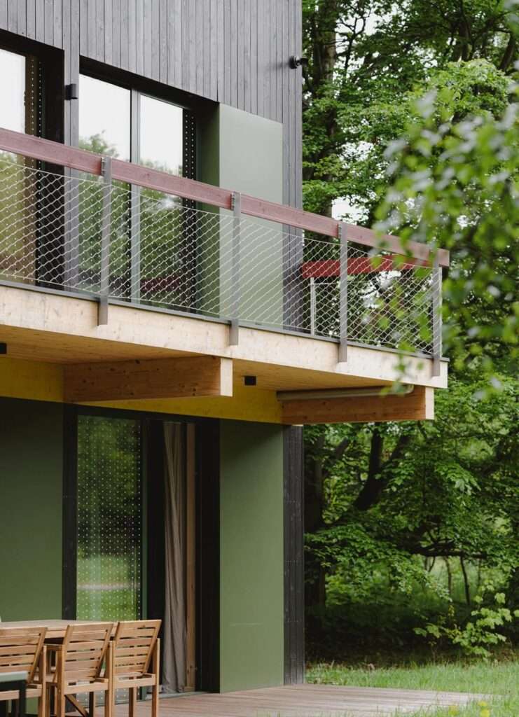 Close-up of a wooden balcony structure with wire mesh railing, yellow beam detail, and dark timber wall.