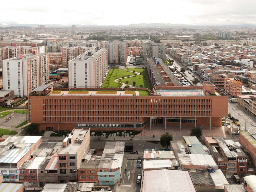 Drone aerial view of the linear red brick Feliza Bursztyn School building integrated adjacent to a public park in Bogotá.