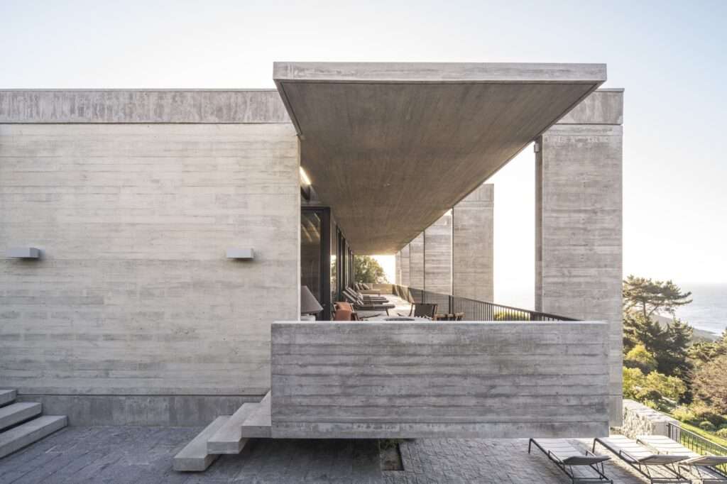 Side view of Casa Zapallar showing the dramatic overhang of the raw concrete roof canopy and access stairs.