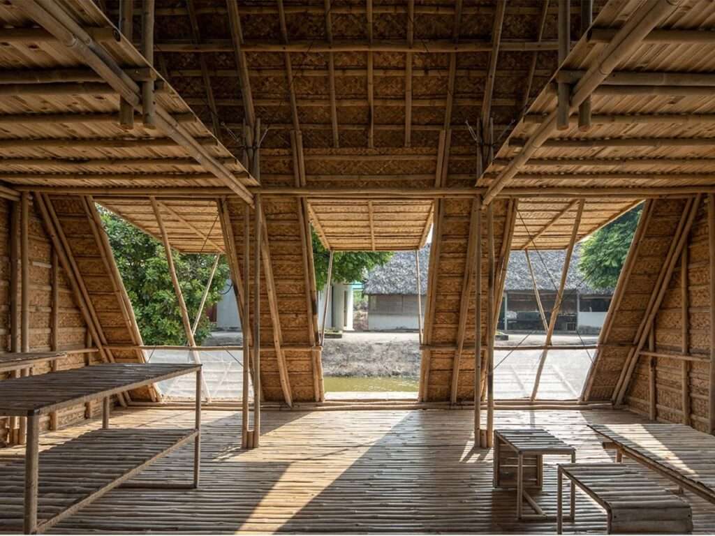 Closer interior view of the Floating Bamboo House, with bamboo benches and tables on the woven floor, looking through large raised bamboo shutters to the opposite river bank.