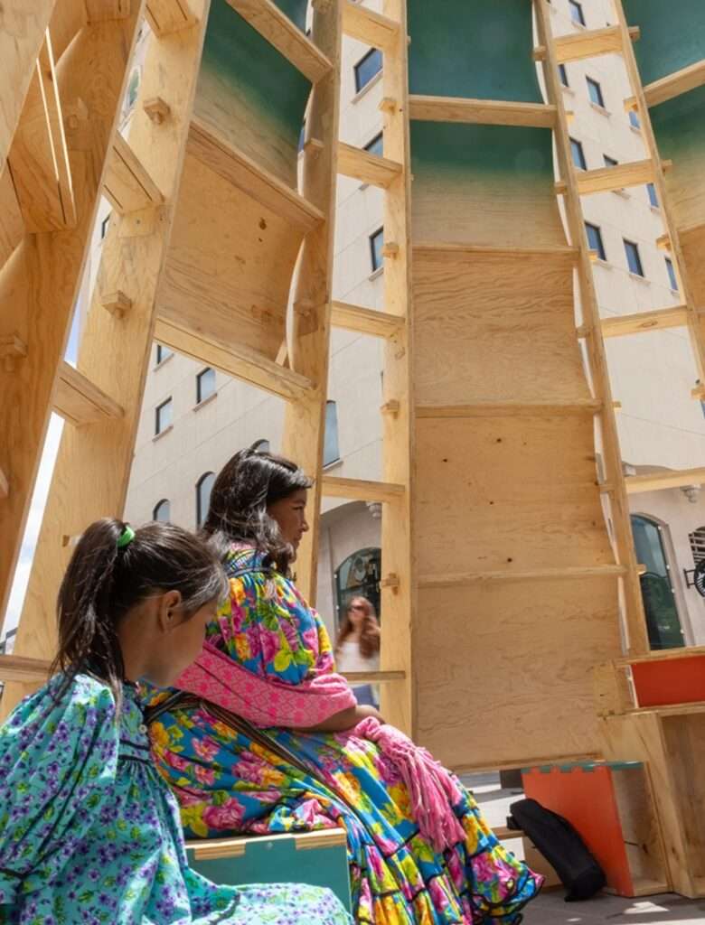 Close-up view of visitors seated inside the Paso Nara temporary architectural pavilion.