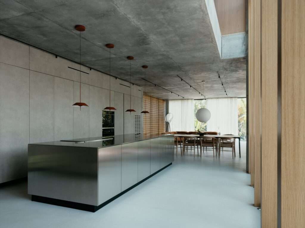 Minimalist kitchen featuring a seamless stainless steel island, integrated wall panels, and suspended reddish pendant lights.