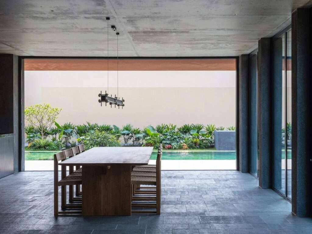 Ground floor dining area with a long wooden table opening to an outdoor garden and swimming pool through sliding glass doors.