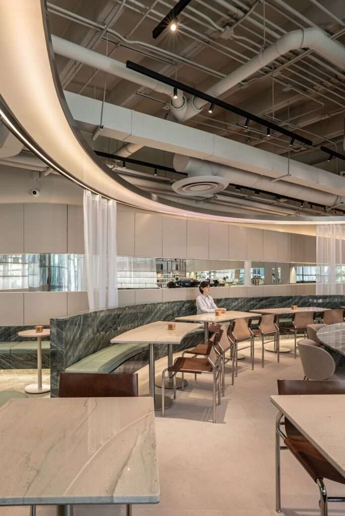 Green quartzite stone bench, beige tables, and overhead curved light element at Raheeq Ohm dining area.