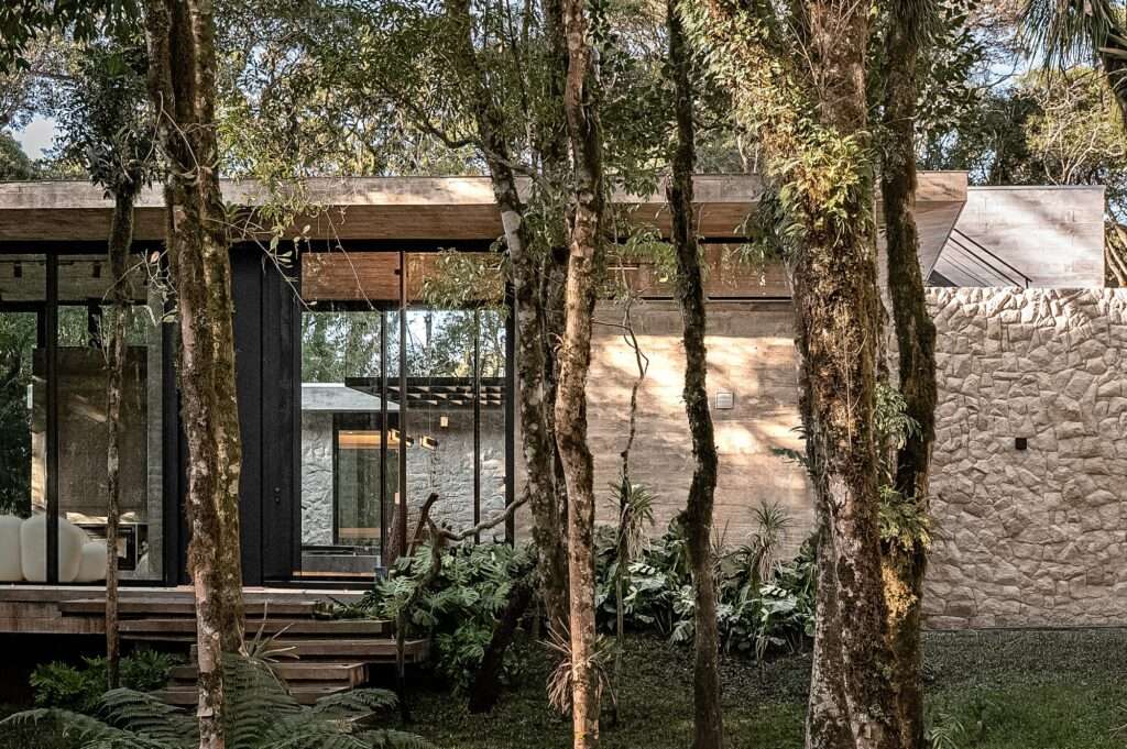 Side exterior angle showing a textured natural stone wall adjacent to full-height sliding glass doors and concrete steps.