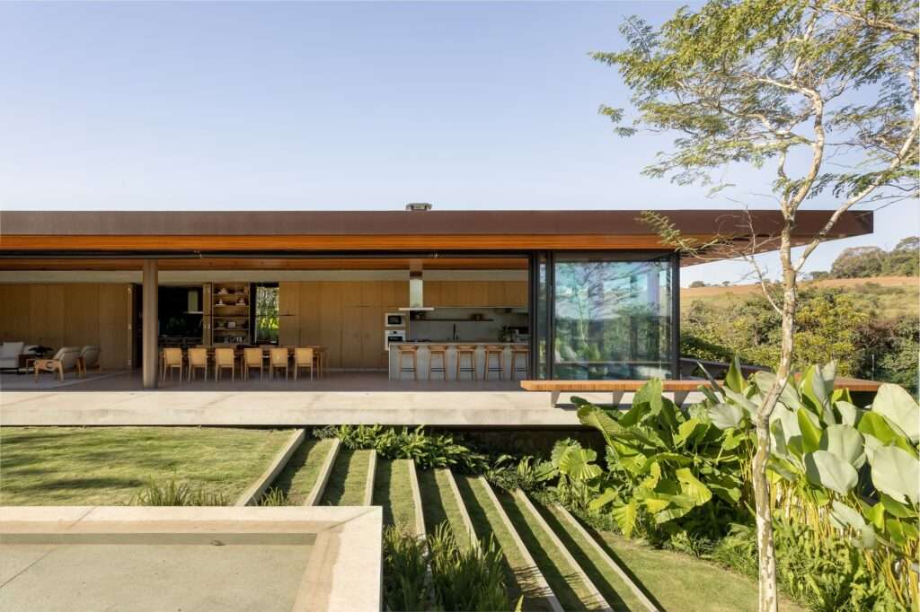 Exterior view of Casa da Mata showing an open living pavilion opening to a stepped lawn terrace and dense tropical foliage.