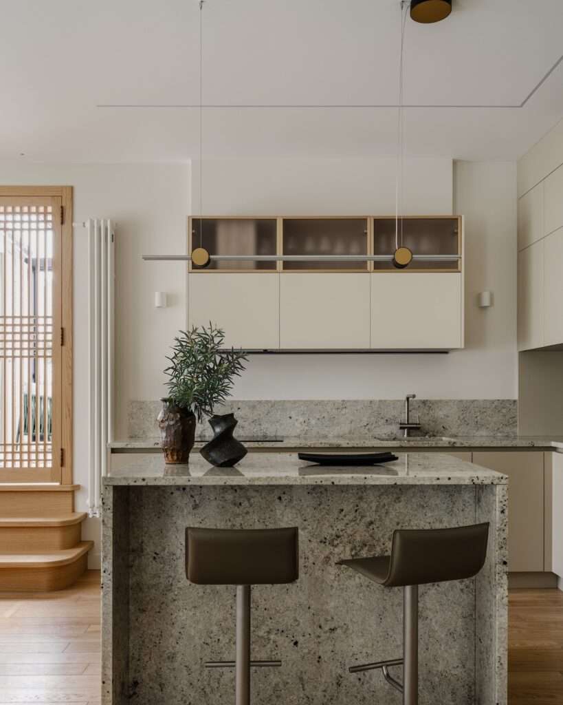 Kitchen island made of textured grey granite paired with modern leather barstools and minimal linear pendant lighting.