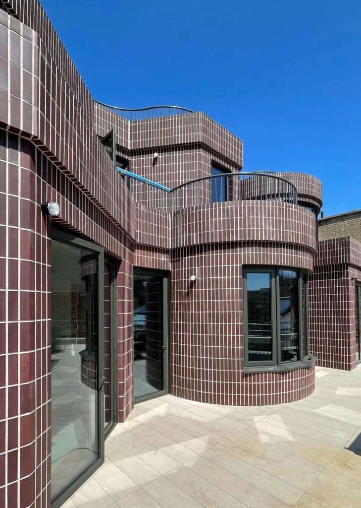 Close-up of dark purple bricks laid vertically on edge along the curved facade and terrace walls of Smart's Place.