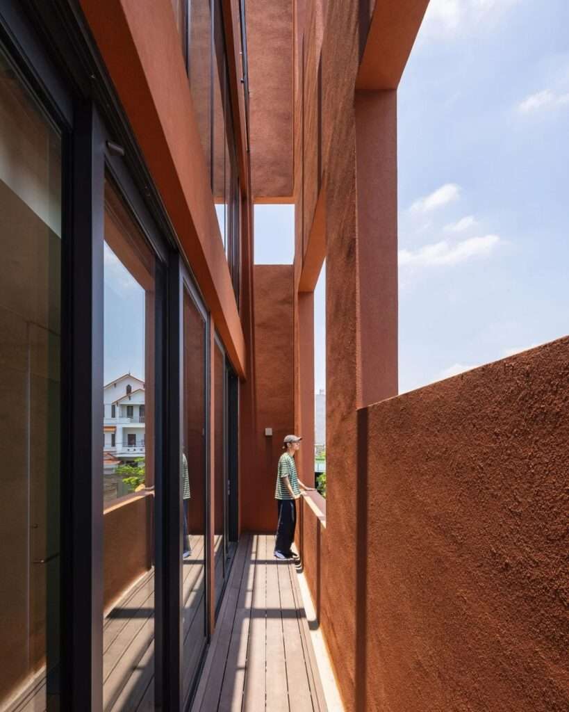 Narrow corridor balcony situated between the glazed interior wall and the outer terracotta screen wall.