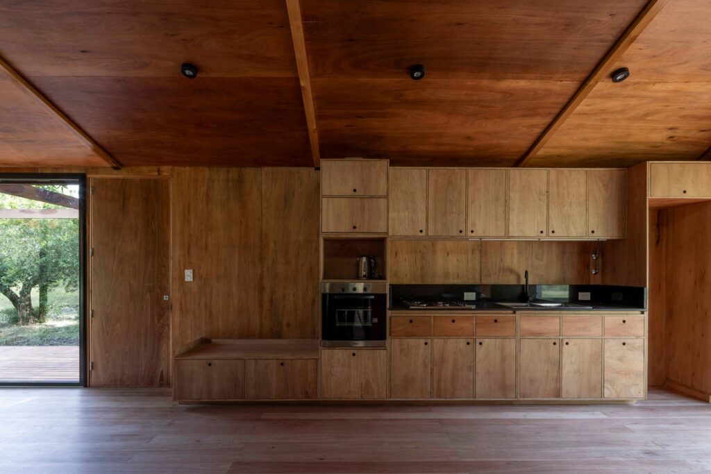 Minimalist custom wooden kitchen cabinets and integrated appliances built into a plywood-paneled wall inside Etchegoyen House.